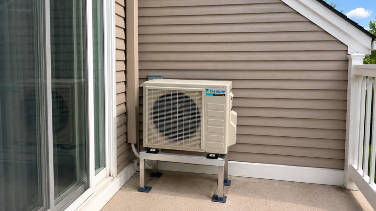 Daikin mini-split outdoor unit mounted on a metal stand beside a sliding patio door.