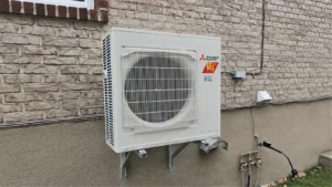 Mitsubishi Electric heat pump outdoor unit mounted on brackets against a brick exterior wall.