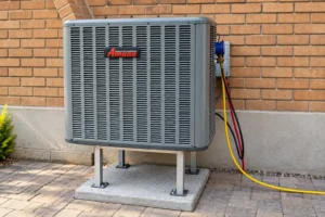 Amana outdoor air conditioning unit mounted on a raised stand beside a brick wall.