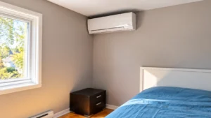 Wall-mounted mini-split air conditioner installed above a bed in a bright modern bedroom.