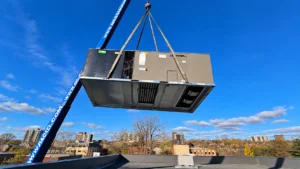 Commercial rooftop HVAC unit being lifted by a crane above an urban building
