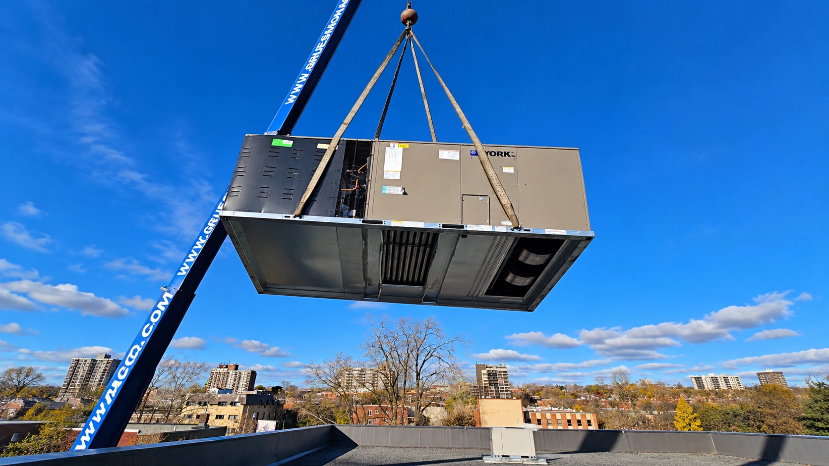 Commercial rooftop HVAC unit being lifted by a crane above an urban building