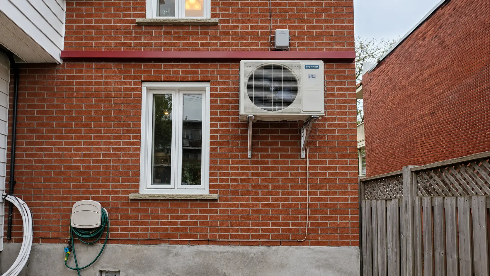 Franklin outdoor heat pump mounted on a red brick house wall beside white-framed windows.