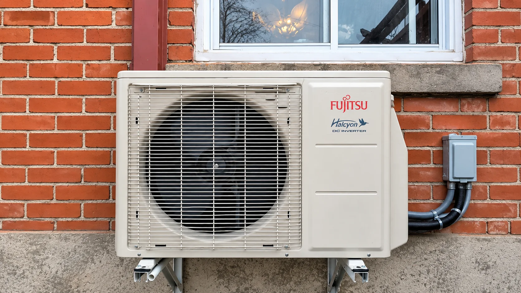 Fujitsu Halcyon outdoor heat pump unit mounted on brackets beside a red brick wall and window.