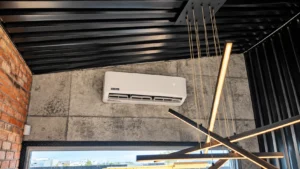 Goodman wall-mounted mini-split air conditioner installed on a concrete wall beneath a black industrial ceiling.