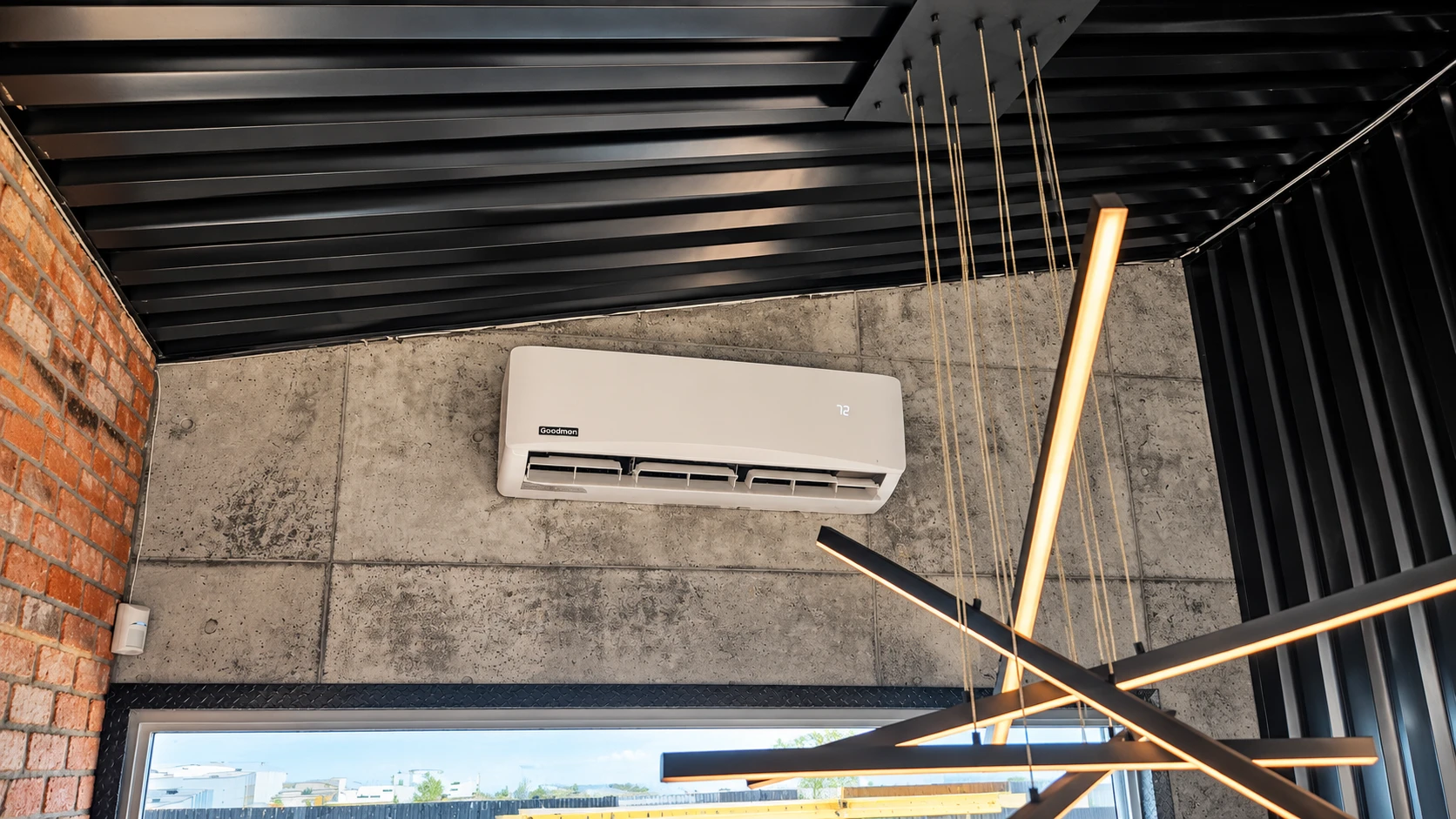 Goodman wall-mounted mini-split air conditioner installed on a concrete wall beneath a black industrial ceiling.